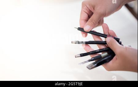 Mano femmina che tiene gli attrezzi per cucire i prodotti di cuoio. Portafogli fatti a mano, cinture, borse su fondo di vestiti di cotone bianco. Foto Stock