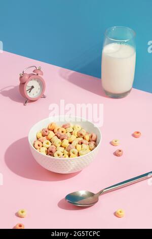 Anelli di grano colorati in una ciotola bianca su tavola rosa. Cibo per la colazione per bambini Foto Stock