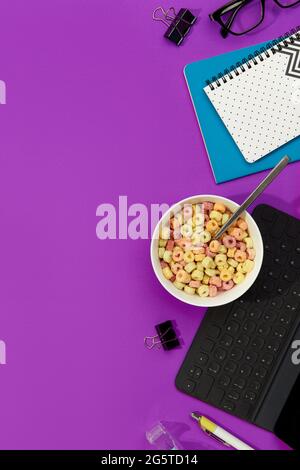 Anelli di grano colorati in una ciotola bianca con cancelleria sul tavolo viola Foto Stock