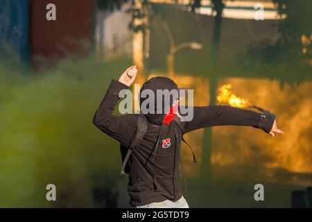 Medellin, Antioquia - Colombia il 28 giugno 2021. Un dimostratore getta una roccia alla polizia mentre una bomba molotov vola dietro di lui mentre le proteste anti-governative si scatenano in scontri tra dimostranti e la polizia in rivolta della Colombia (ESMAD), tra tensioni politiche contro il governo del presidente Ivan Duque, Casi di brutalità e disuguaglianze della polizia mentre la Colombia segna un secondo mese di proteste anti-governative, in ,Medellin, Antioquia - Colombia il 28 giugno 2021. Foto Stock