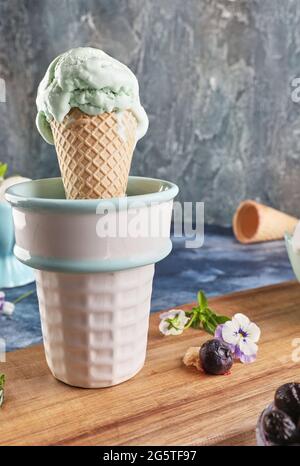 Gelato al pistacchio nel cono del waffle e vase su sfondo blu Foto Stock