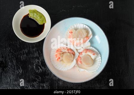 Capesante grezzo naturale con gamberi bolliti nel lavandino in una ciotola di ceramica con salsa di soia e wasabi su fondo scuro. Messa a fuoco selettiva. Foto Stock