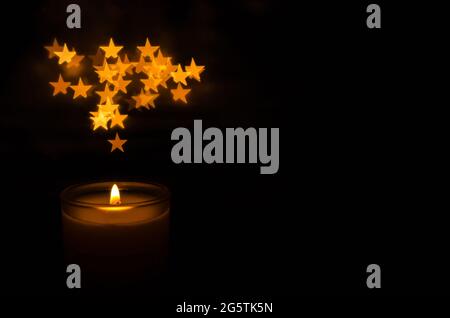 Candela aromatica con fiamma e bokeh a forma di stella su sfondo scuro per ringraziamento e giorno di Natale. Foto Stock