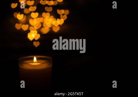 Candela aromatica con fiamma e forma d'amore bokeh su sfondo scuro per ringraziamento e giorno di Natale. Foto Stock