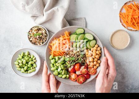 Le mani della donna tengono la ciotola del buddha, il pasto equilibrato vegano con i fagioli, i ceci e le verdure. Vista dall'alto. Perdita di peso, concetto di consumo pulito Foto Stock