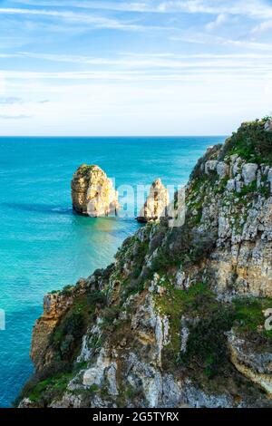 Scogliere rocciose con fresca vegetazione verde e soleggiato cataste di mare nell'oceano turchese alla costa di Lagos, Portogallo - orientamento verticale Foto Stock