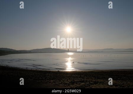 Sole che sorge dietro la città di Swansea dall'altra parte della baia in una giornata azzurra Foto Stock