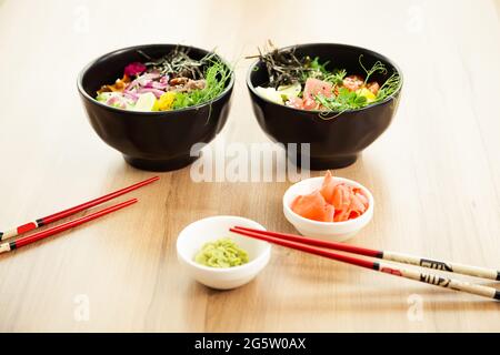 Due insalate di poke con manzo e tonno in una ciotola con varie salse sul tavolo del ristorante. Poke insalate in una ciotola accanto a chopsticks e zenzero con Foto Stock
