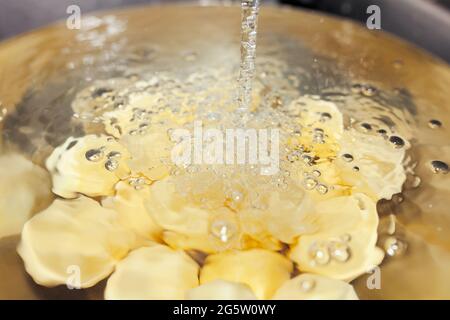 Patate crude sbucciate sotto l'acqua corrente in ciotola cromata nel lavandino Foto Stock