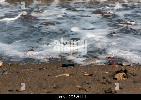 spiaggia di sabbia e ciottoli bagnata dalla schiuma di un'onda che si avvicina con dettagli e texture. Foto Stock