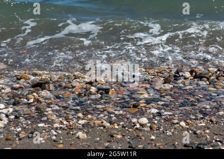 spiaggia di sabbia e ciottoli bagnata dalla schiuma di un'onda che si avvicina con dettagli e texture. Foto Stock