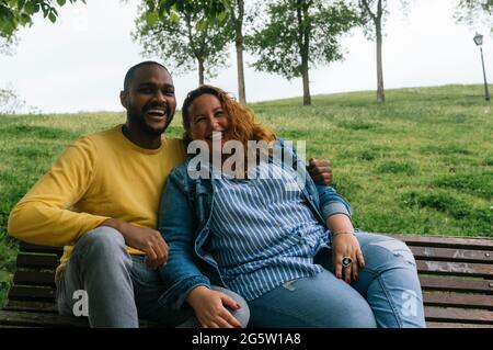 Giovane coppia interracial in amore baciando e ridendo in un parco Foto Stock