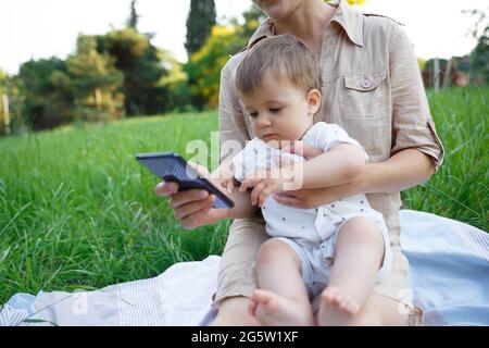 piccolo ragazzo seduto sul grembo della mamma che tira al phon mobile. Foto Stock