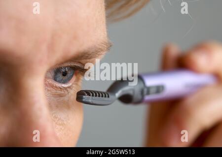giovane caucasica modello femminile reale con occhi blu utilizzando un arricciacapelli portatile elettrico riscaldato eyelash primo piano Foto Stock