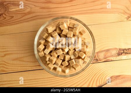 Cubetti di zucchero di canna in un recipiente di vetro, primo piano, su un tavolo di legno, vista dall'alto. Foto Stock