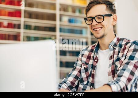 Giovane uomo d'affari sorridente, usa il laptop, l'uomo lavora su internet seduto ad un tavolo con un computer portatile moderno in un bar sullo sfondo o Foto Stock