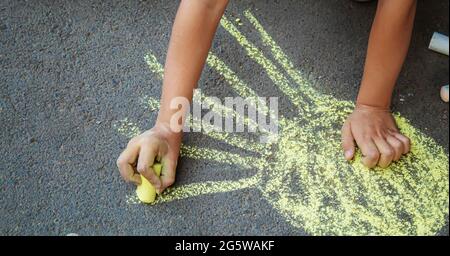 Bambino disegna con un gessetto sul marciapiede. Messa a fuoco selettiva. Foto Stock