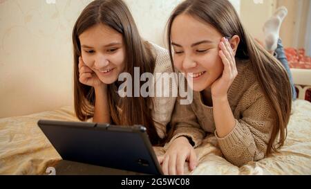 Ritratto di due ragazze adolescenti sorridenti che hanno una videoconferenza su un computer tablet mentre si trovano a letto. Foto Stock