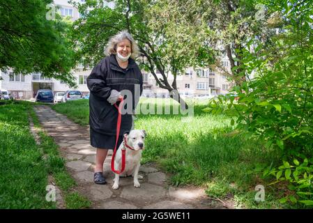 Donna anziana sorridente su una passeggiata con un cane su Leash Foto Stock