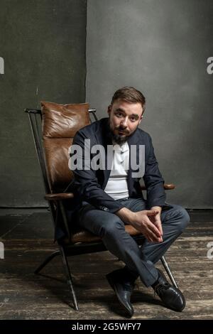 Un giovane brutale uomo si siede su una sedia. Foto di alta qualità Foto Stock