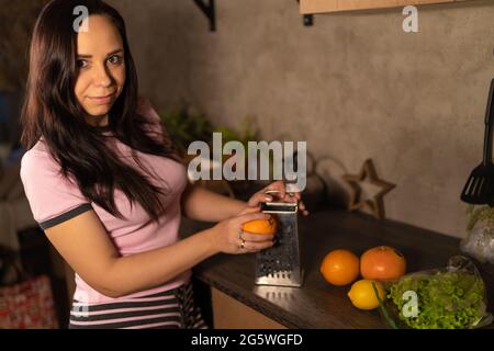 Le mani delle donne fanno la scorza d'arancia in cucina. Foto Stock