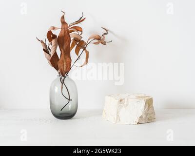 Podio grigio in pietra naturale su sfondo bianco, piattaforma per l'esposizione dei prodotti e rami autunnali in vaso. Vuoto per il design mockup. Vista frontale. Copia spa Foto Stock