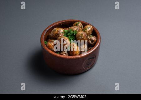 primo piano di patate arrostite con erbe in ciotola di argilla su sfondo nero Foto Stock