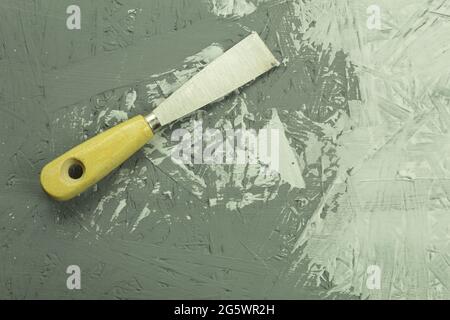 Cazzuola da costruzione sul tavolo durante il processo. Processo di ristrutturazione, sfondo con spazio per la copia. Coltello per stucco in un mastice sullo sfondo della parete Foto Stock