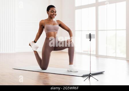 Donna nera che allunga la gamba davanti allo smartphone sul treppiede Foto Stock