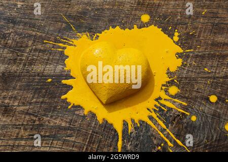 Cuore giallo. forma tridimensionale del cuore su tavola in legno naturale frantumata da vernice gialla. Foto Stock