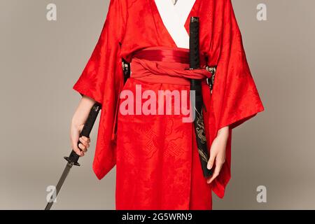 Vista tagliata della donna in kimono che tiene la spada isolata sul grigio Foto Stock