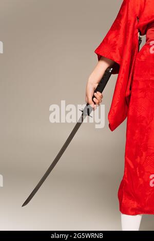 Vista tagliata della donna in kimono orientale tenendo la spada isolata sul grigio Foto Stock