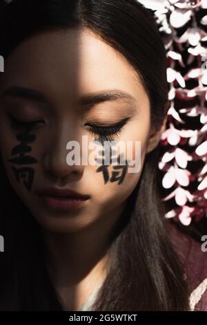 Geroglifici di fronte alla giovane donna asiatica in luce isolata su nero Foto Stock