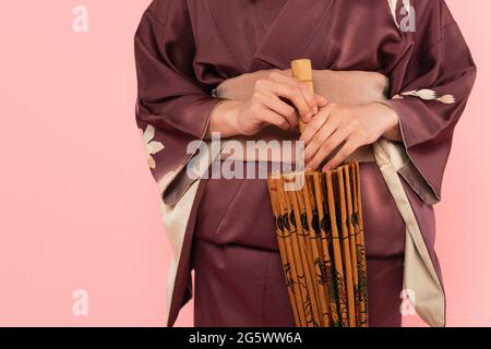 Vista tagliata di donna in kimono che tiene l'ombrello giapponese isolato su rosa Foto Stock