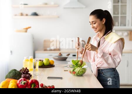 Ritratto di giovane donna sorridente che cucinava insalata fresca in cucina Foto Stock