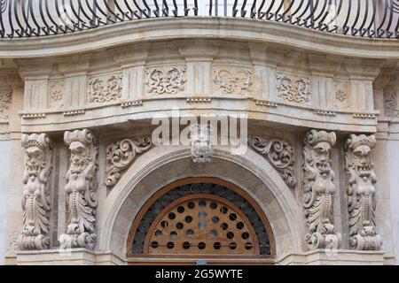 Noto, Siracusa, Sicilia, Italia. Grottesche figure scolpite su façade ornamentali fiammeggianti di uno storico palazzo barocco in corso Vittorio Emanuele. Foto Stock