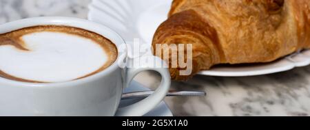 Classica colazione italiana Cappuccino e Cornetto su tavolo in marmo in un bar Foto Stock
