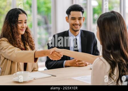 Closeup handshake dopo intervista accordo tra giovane donna asiatica e due manager con movimento positivo in sala riunioni, handshake con manager, Bu Foto Stock