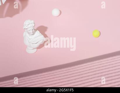 Composizione astratta con la scultura di testa di un antico Apollo e palle da tennis bianche e gialle su uno sfondo di luce del sole rosa pastello. Arte concettuale Foto Stock