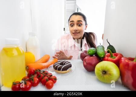 Una donna divertente ed eccitata che guarda la vista delle ciambelle dal frigorifero Foto Stock