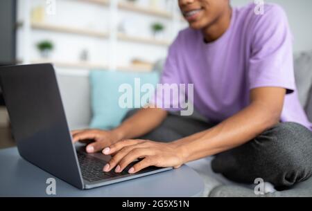 Concetto di e-learning. Adolescente afroamericano che studia online, digitando sul computer portatile a casa, closeup delle mani Foto Stock