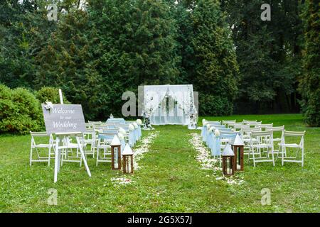 Decorazioni per cerimonie nuziali: Arco, sedie, puntatore e un sacco di fiori in stile bianco e blu, su uno sfondo di verde Foto Stock