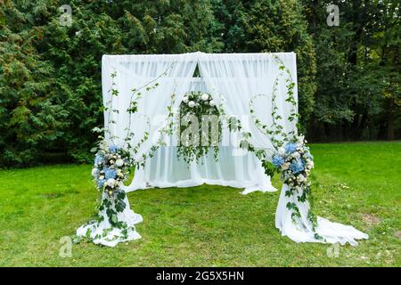 Decorazioni per cerimonie nuziali: Arco, sedie, puntatore e un sacco di fiori in stile bianco e blu, su uno sfondo di verde Foto Stock