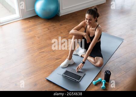 Giovane donna sdraiata sul tappetino yoga usando il computer portatile Foto Stock