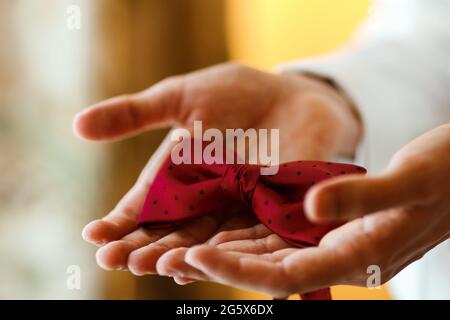 Giovane sposo che tiene in mano una cravatta rossa punteggiata. Primo piano degli accessori per matrimoni da uomo Foto Stock