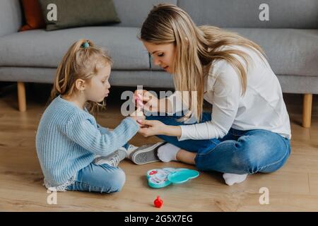 Madre e piccola figlia dipingono le unghie con smalto giocattolo. Capretto che gioca con la mamma a casa. Concetto di buona parenting e felice infanzia, famiglia Foto Stock