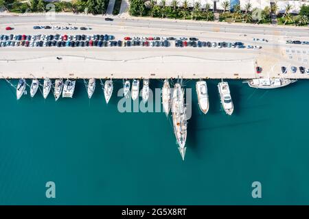 Porto marina in basso. Nafplio città, Grecia, vista aerea drone. Barche a vela e yacht ormeggiati al porto, calmo sfondo blu mare. Vela Egeo se Foto Stock