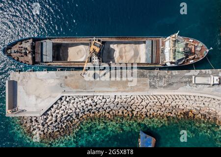 Attrezzature e macchinari per la costruzione di opere marine, drone aereo vista dall'alto, macchina per il carico di sabbia su una nave al porto di Korissia, isola di Kea Tzia, Cycla Foto Stock