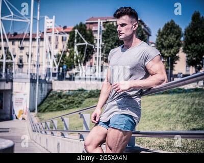 Bel giovane uomo in forma in t-shirt grigia, all'aperto in città Foto Stock