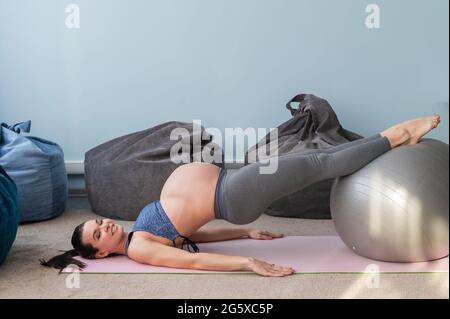 Donna europea incinta esegue esercizi con palla fitness. La madre in attesa sta facendo yoga nel 3° trimestre. Ragazza in classe in Foto Stock